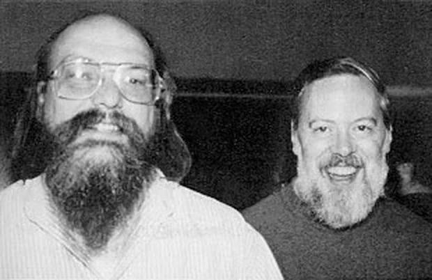 A black and white photograph of two bearded men in the 1970s, one wearing glasses, both looking at the camera.